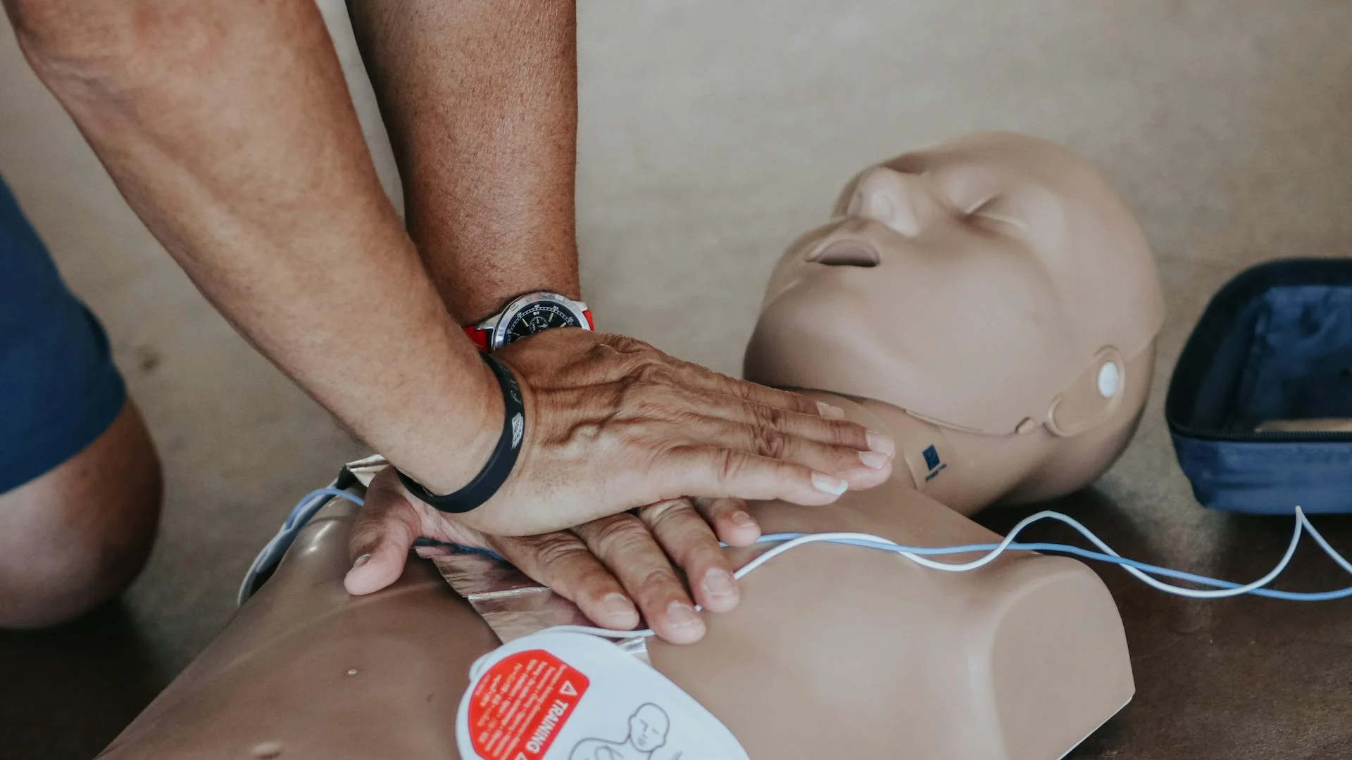 Hands performing CPR on training mannequin during AED training certification course